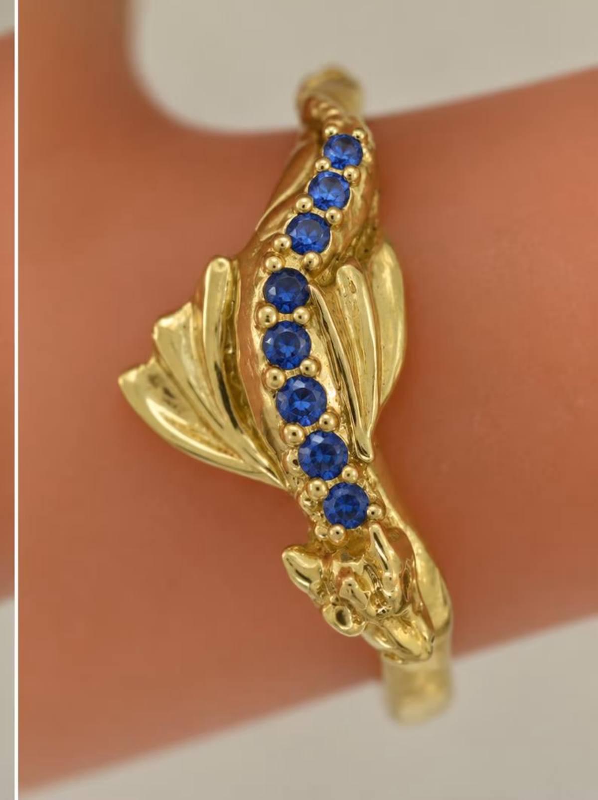 Solid gold Baby Dragon ring with eight natural blue sapphires along its back, shown on a finger with sculpted wings and dragon face.
